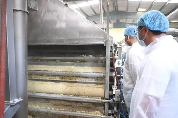 Two men in white coats standing in front of a machine, possibly used for cooking and mashing potatoes.
